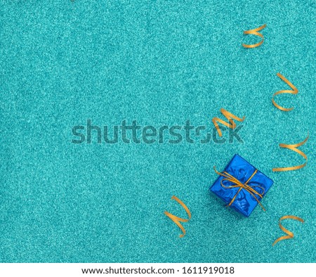 Wrapped classic blue gift box with gold ribbon on blue background with bright party streamers. Birthday, party, fun, joy concept. Greeting, invitation card. Flat lay, top view, copy space.