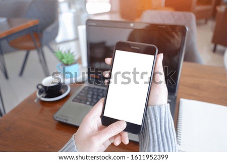 Mockup picture of business woman’s hands or man's hands holding smart phone with white blank screen in modern place.
