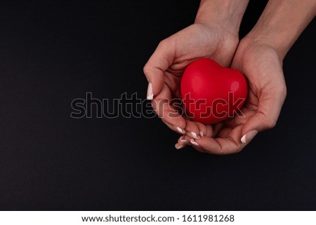 Female hands give a red heart on a black background
