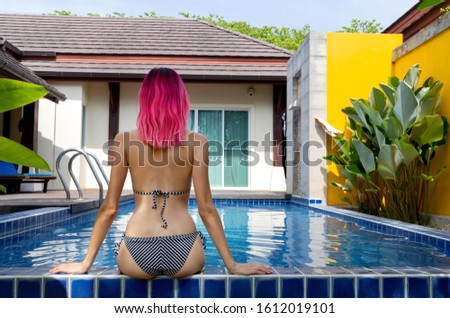 Young woman with vibrant pink hair relaxing in swimming pool at spa resort. Back view. Travel vacation concept.