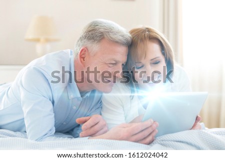 Senior couple looking at their old pictures on digital tablet in bed
