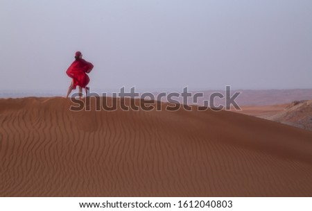 Woman in red on a dune in the desert. UAE