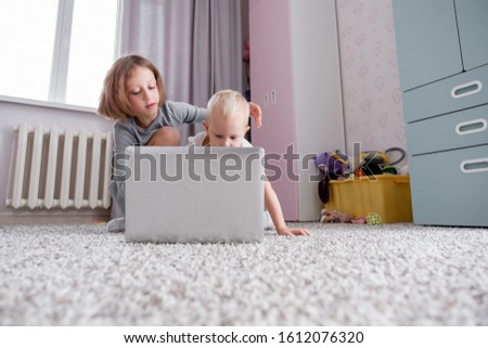 Brother and sister are watching cartoon on laptop while lying on floor in children's room. Concept of friendly enthusiastic smart little children. Children and social addiction. Copyspace