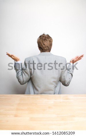Unrecognizable businessman in gray suit shrugging and holding up his hands while facing the wall