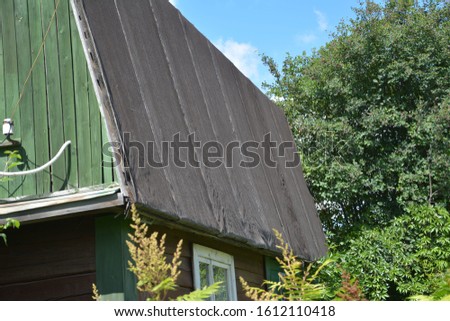 Fragments of the roof of a small summer cottage before repairing the worn roof. The old roof of the cottage is made of flexible roofing material. On a Sunny summer day.