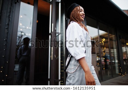 African american woman in overalls and beret walking out the door in outdoor terrace with christmas decorations.