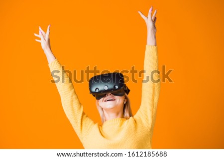 Computer game player uses virtual reality. A young woman in a VR helmet, passionate about the game, portrait on a yellow background