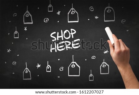 Hand drawing SHOP HERE inscription with white chalk on blackboard, online shopping concept