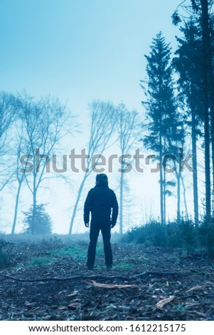 Man in black jacket and trousers in foggy winter forest.