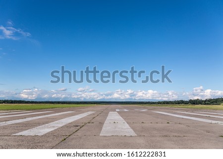 The runway of a rural small airfield against a blue sky with clouds of the airfield. Royalty-Free Stock Photo #1612222831