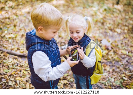 Children preschoolers Caucasian brother and sister take pictures of each other on mobile phone camera in forest park autumn. theme of hobby and active lifestyle for child. Profession photographer.