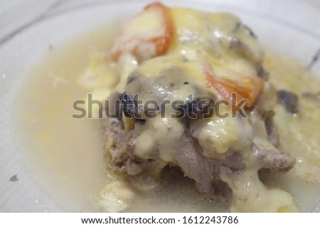 Food photo of a meat casserole with tomatoes, mushrooms, cheese and gravy in a round glass plate on a background of an old wooden table with shabby white paint.
