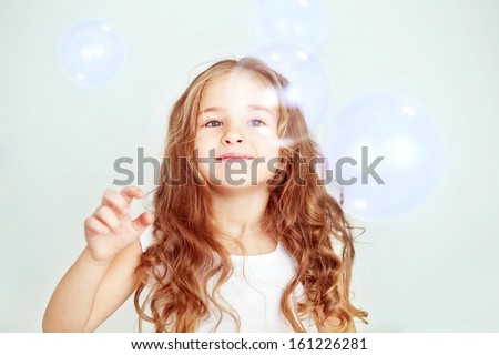 Funny lovely little girl in white dress playing with soap bubbles