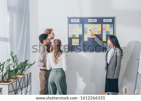 attractive asian scrum master pointing at db design letters on sticky note near businessmen and businesswoman Royalty-Free Stock Photo #1612266331