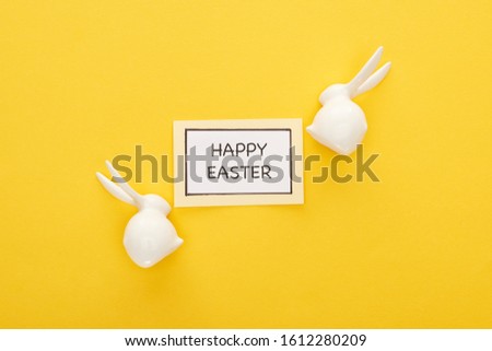 top view of greeting card with happy Easter lettering near Easter white bunnies on yellow colorful background