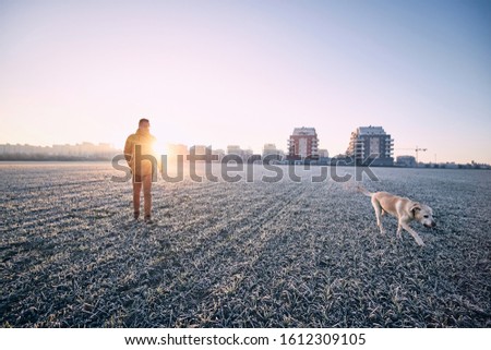 Frosty morning with dog. Young man walking with his labrador retriever against cityscape at sunrise. Prague, Czech Republic