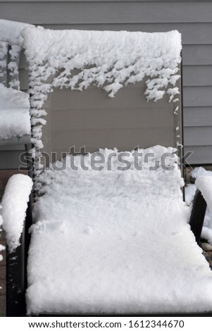 A tan, mesh, patio chair covered in snow after an early snowfall in autumn in Wisconsin, USA