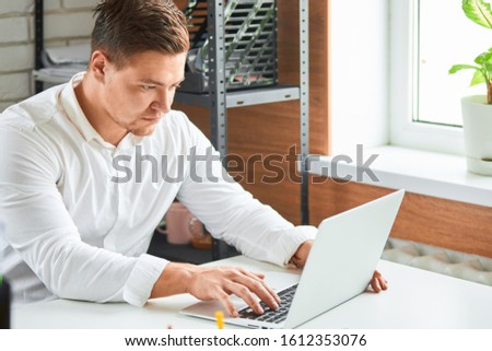 Confident and concentrated businessman wearing white shirt sit looking at laptop and typing, business male. Office background
