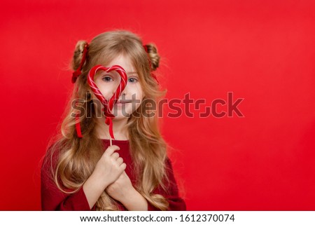 So cute, cute and funny! Portrait of a beautiful sweet girl in a red dress, she dreams of pastry and pastry isolated on a red background