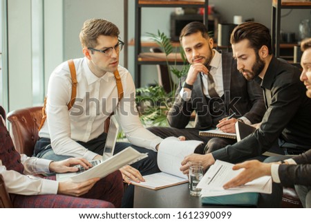 young caucasian business partners sharing and commenting reports. holding papers and notebooks, making notes and keep records of their market, in formal wear, isolated in modern office
