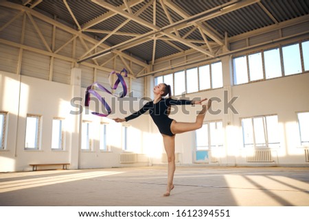 Graceful, charming female gymnast, making grand battement jete balance, waving long coloured ribbon in the air, dancing on floor, shot from below