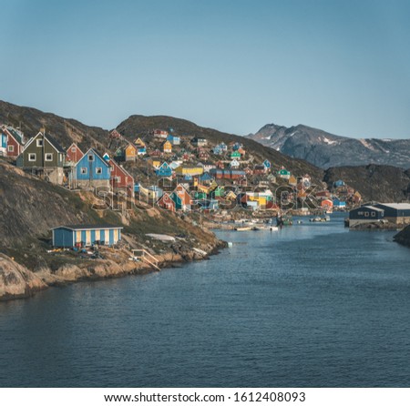 Colorful houses dot the hillsides of the fishing town of Kangaamiut, West Greenland. Icebergs from Kangia glacier in Greenland swimming with blue sky and clouds. Symbol of global warming.