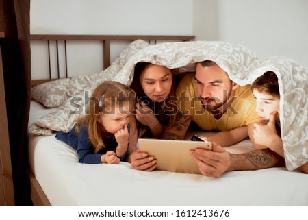parents spend time together at home with children, lying on bed under duvet, in casual wear