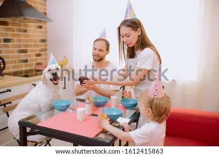 happy cheerful friendly caucasian family celebrating birthday together with their domestic animal white dog, lovely pet and his owners at home. Isolated in light kitchen