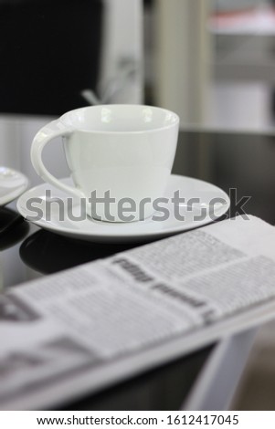 pictured is an image of a white cup and newspaper on a black table