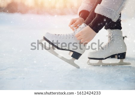 Girl ties shoelaces on white figure skates for ice rink in winter. Christmas holidays concept.