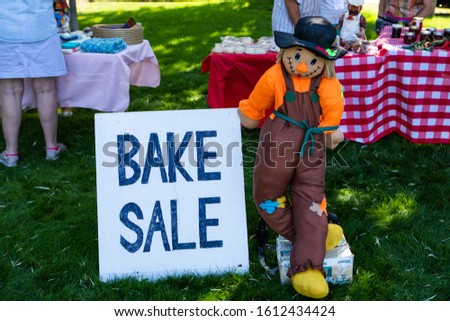 Farmer doll holds Bake Sale sign at outdoors. Different bakery products and sweets on table. Bakery fair in Okanagan Valley, British Columbia, Canada