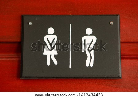 Close-up view of gentleman and lady toilet signs. Restroom funny signs hanged on the wooden red door. Men and women WC sign for the washroom