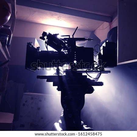 Mystical silhouette of a movie camera in the sun's rays of light from the window. Camera on a tripod in standby mode