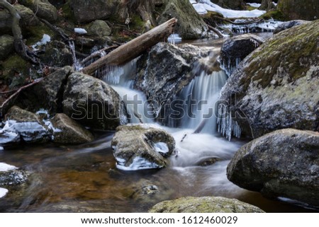 Frozen brook and waterfalls with icy pieces. Winter mountain nature in forest.
