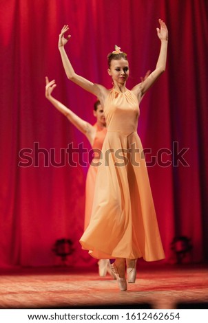 Young women ballerinas in yellow and orange long dresses perform a ballet performance on stage at the theater