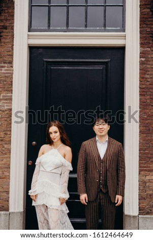 Loving couple on the background of the doors of the house. A guy in a brown suit with glasses and a red-haired girl in a white dress.