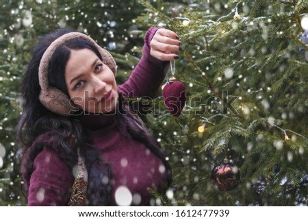 Female hands holds Christmas toy in the shape of a red heart  on the background of a festive Christmas tree. The concept of decorating a Christmas tree, love, New Year and Christmas.