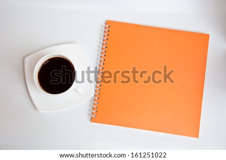 black coffee and orange notebook on white background