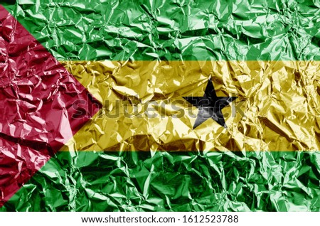Sao Tome and Principe flag depicted in paint colors on shiny crumpled aluminium foil closeup. Textured banner on rough background