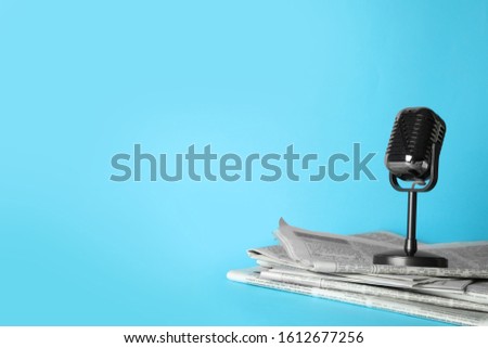Newspapers and vintage microphone on light blue background, space for text. Journalist's work