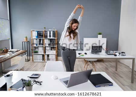 Young Businesswoman Stretching Her Arms At Desk Royalty-Free Stock Photo #1612678621