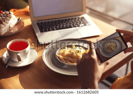 Young blogger taking picture of pasta at table in cafe, closeup