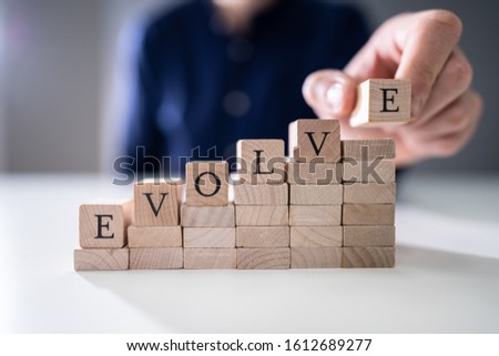 Close-up Of Person's Hand Placing Last Alphabet Of Word Evolve On Wooden Block Royalty-Free Stock Photo #1612689277