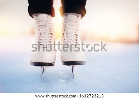 Winter active holiday concept. Woman standing on ice in white figure skates, snow flakes sunset.