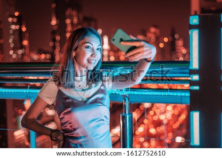 A girl takes a selfie against the background of a night city with skyscrapers