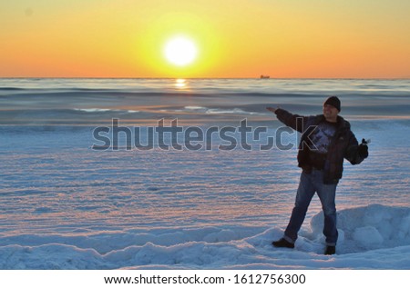 Image of a man standing on the icy shore of the winter sea at sunset.