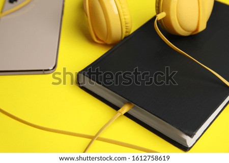 Book, modern headphones and smartphone on yellow background, closeup