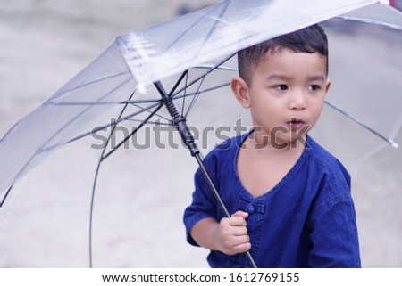 Portrait of little cute boy in blue T-shirt holding an umbrella.                           
