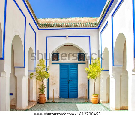Courtyard at white islamic house with blue gate. There are white walls and columns with blue signs and blue doors.