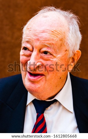 Portrait of happy white elderly man with dark suit, white shirt and striped blue red tie smiling on bright brown background